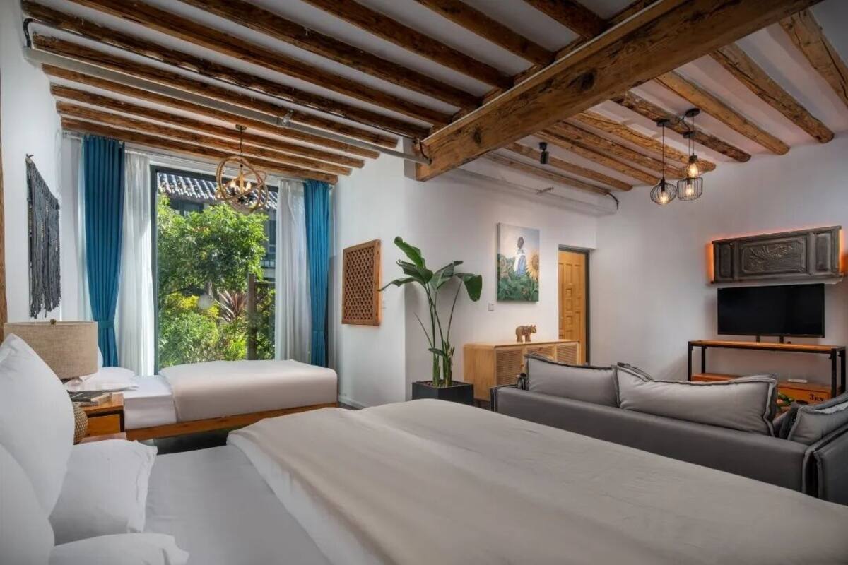 Un dormitorio con una cama grande, un sofá, un televisor y un ventanal con cortinas.