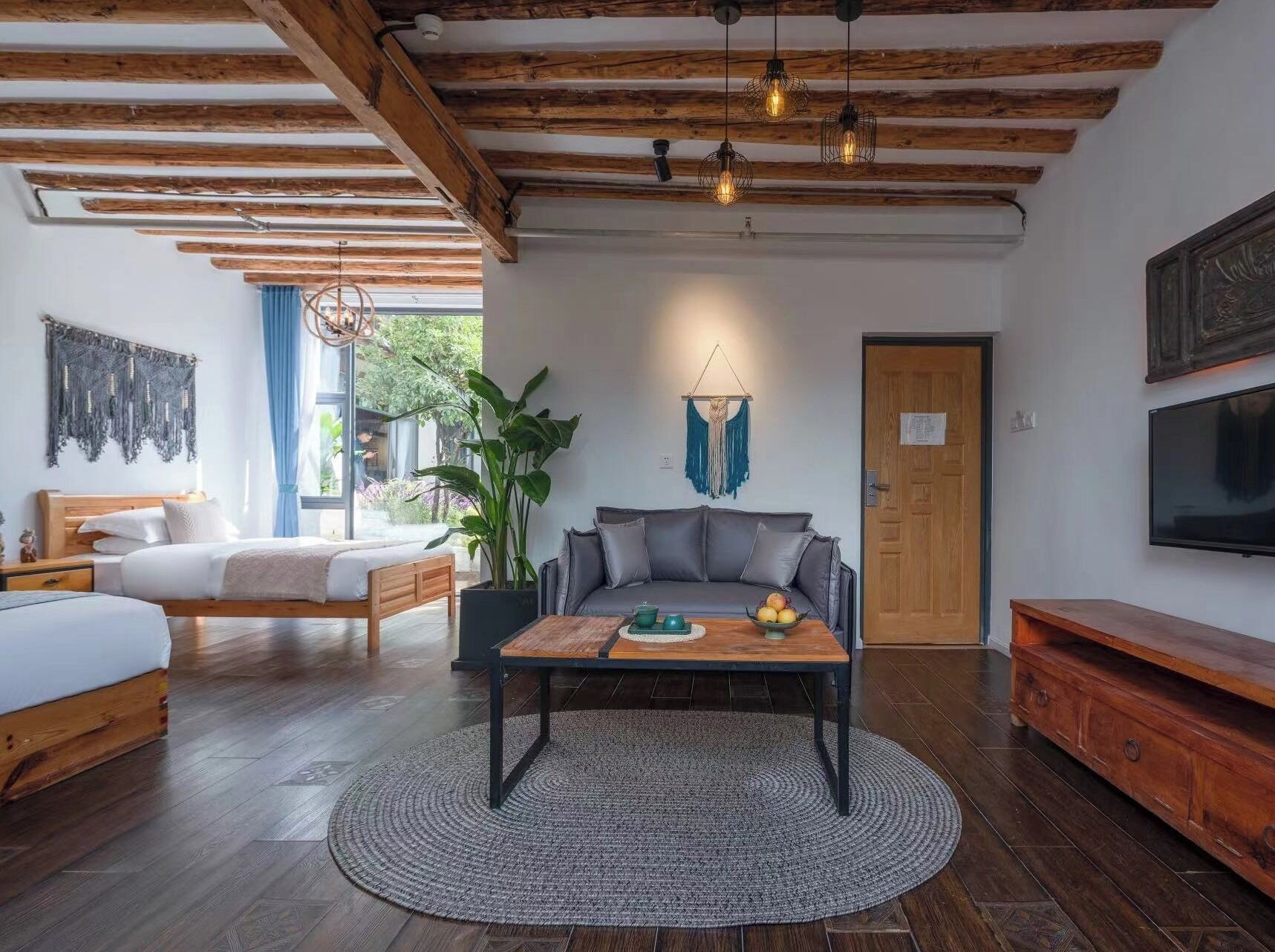 A cozy room with a wooden ceiling, a bed, a sofa, a coffee table with fruit, and a TV on the wall.