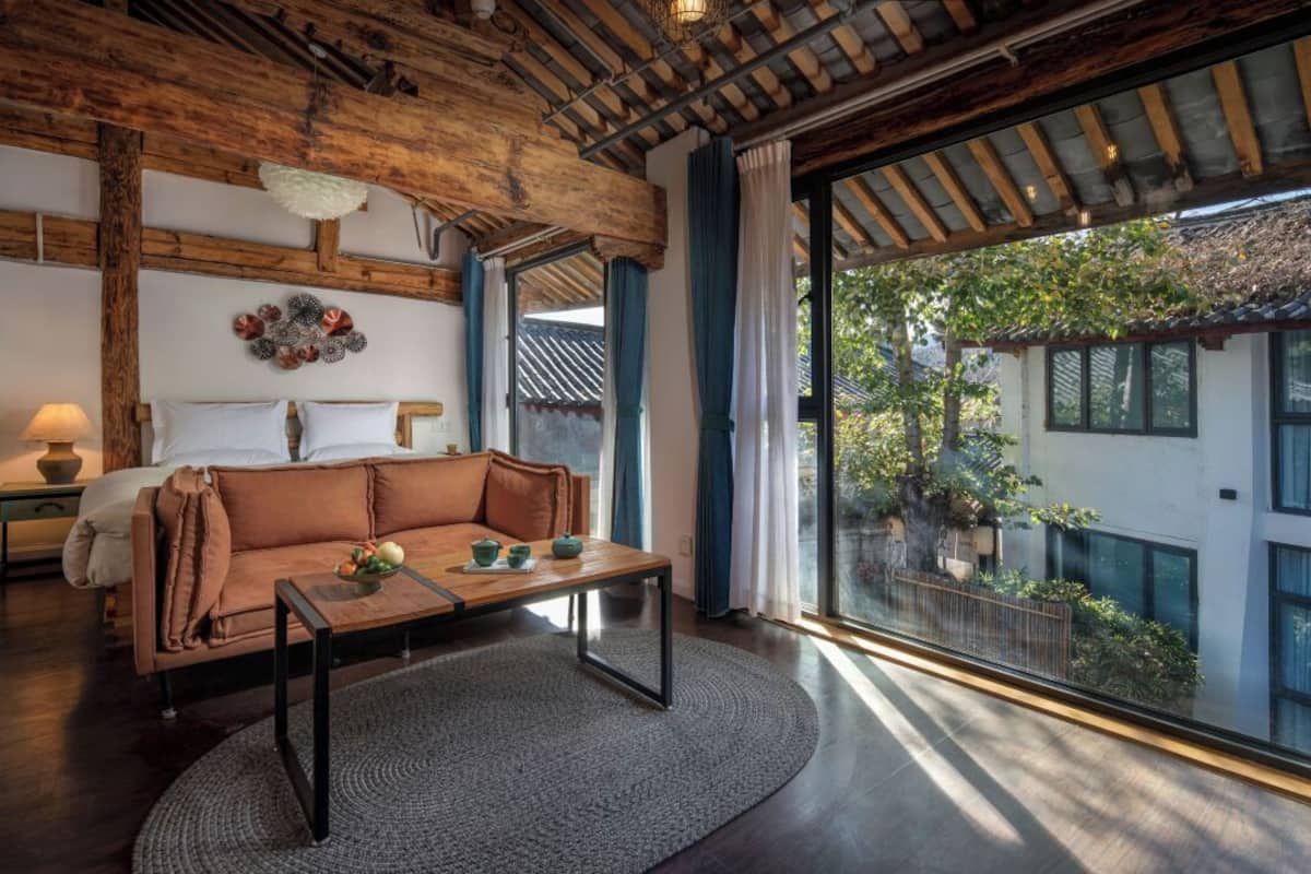 Una habitación acogedora con techo de madera, un sofá, una mesa de centro y vistas a un jardín a través de amplios ventanales.