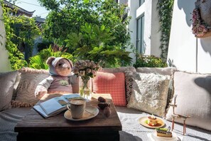 A cozy outdoor seating area with a wooden table, a teddy bear, a vase with flowers, and a cake on a small stand.