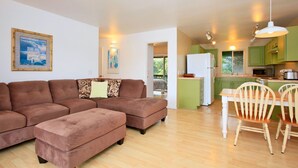 A living room with a brown sectional sofa, a dining table with wooden chairs, and a kitchen area with green cabinets and a white refrigerator. - Yonegan Maui Getaways - Haiku - Unit 2 (Haiku-Pauwela)