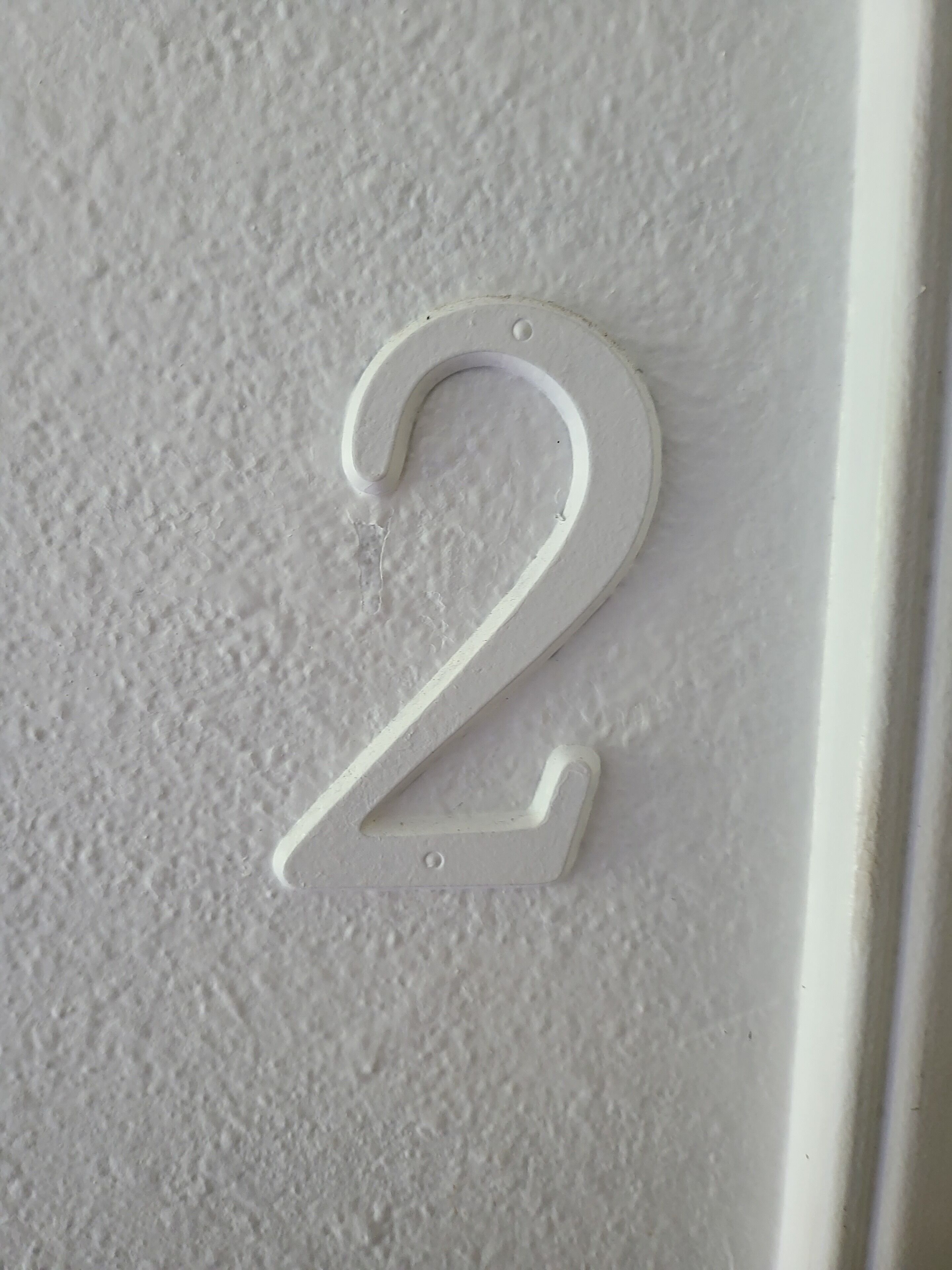 Een wit, in reliëf aangebracht cijfer '2' op een structuurwand.