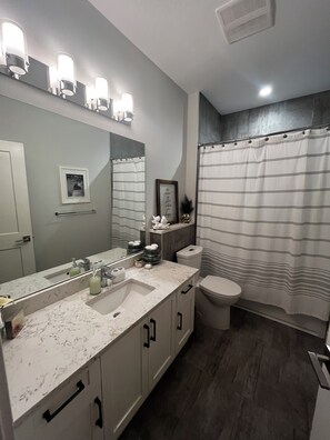 A bathroom with a large mirror, a sink, a toilet, and a shower curtain.