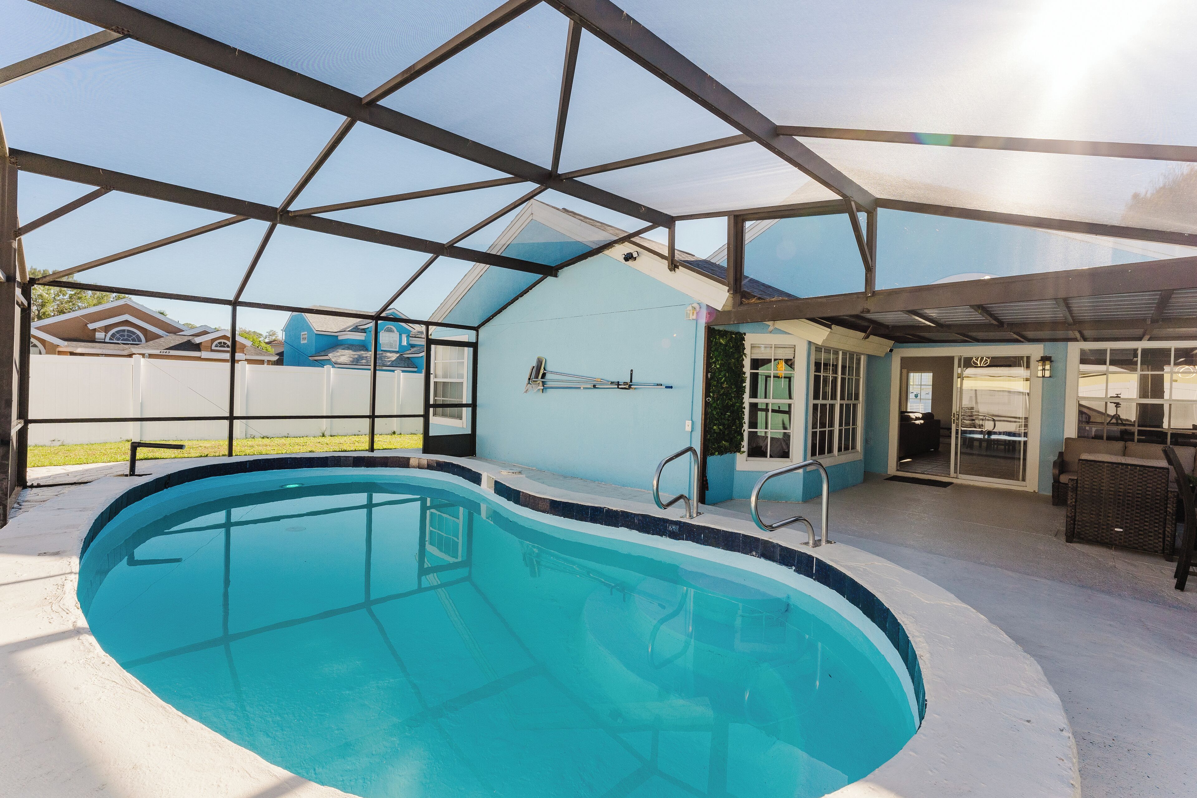 Una piscina con cerramiento de vidrio, un patio cubierto y vistas a un barrio residencial.