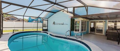 Una piscina con cerramiento de vidrio, un patio cubierto y vistas a un barrio residencial.