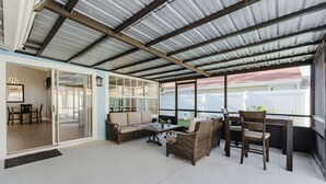 A covered patio area with a sliding glass door leading to a room, furnished with wicker furniture and a small table.