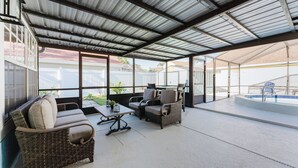 An outdoor patio area with wicker furniture, a pool, and a covered section with a metal roof.