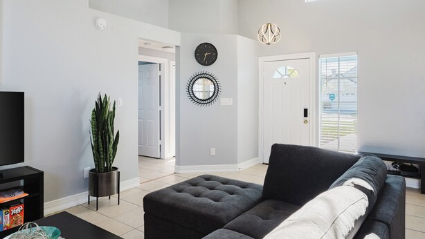 A modern living room with a grey sofa, a potted plant, a black clock, and a decorative wall piece.