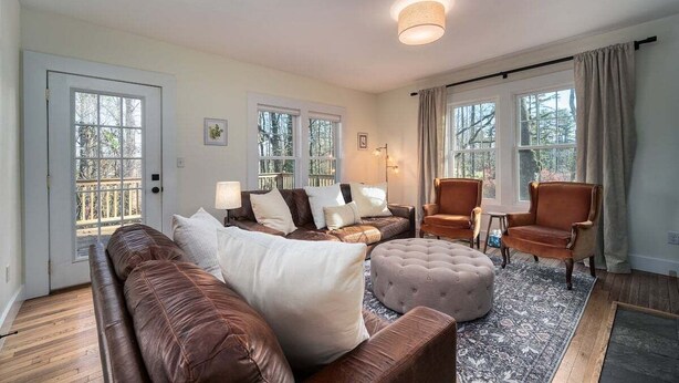 Un salon avec un canapé en cuir marron, un pouf capitonné, un tapis à motifs et un plancher en bois.