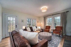 A living room with a brown leather sofa, a tufted ottoman, a patterned rug, and a wooden floor. - Monthly Rental 5 Minutes to Downtown! (Brevard)