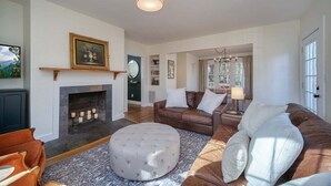Un salon doté d’une cheminée, de canapés en cuir, d’un pouf rond et d’un lustre.