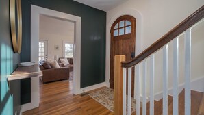 Un couloir doté d’un plancher en bois, d’une porte blanche, d’un mur foncé et d’un escalier avec des rampes blanches.