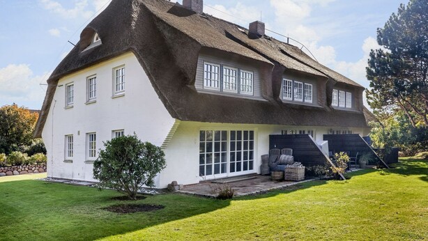 A two-story house with a steeply pitched thatched roof, white exterior walls, and a front porch with outdoor seating. - Green Teft, Whg. 8 - Green Teft - thatched house in the southwest part of the village (Sylt / OT Keitum)