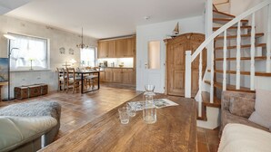 A spacious living area with a wooden dining table, a cozy sofa, and a staircase leading to an upper floor. - Green Teft, Whg. 8 - Green Teft - thatched house in the southwest part of the village (Sylt / OT Keitum)