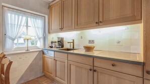 A kitchen with wooden cabinets, a coffee maker, a sink, and a window with curtains. - Green Teft, Whg. 8 - Green Teft - thatched house in the southwest part of the village (Sylt / OT Keitum)