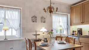A dining area with a wooden table, chairs, a chandelier, and a kitchen in the background. - Green Teft, Whg. 8 - Green Teft - thatched house in the southwest part of the village (Sylt / OT Keitum)