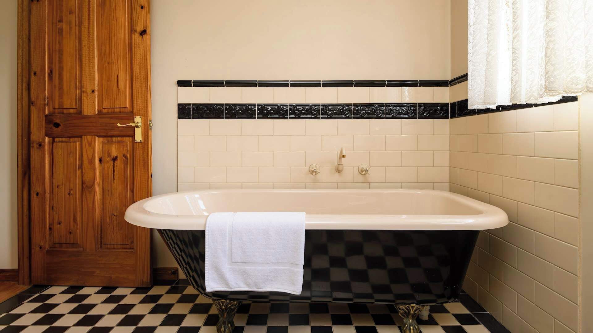Ein Badezimmer mit einer freistehenden Badewanne, einer Holztür und Schachbrettfußbodenfliesen.