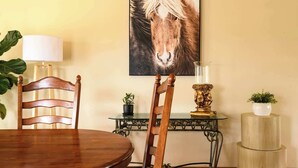 A dining area with a wooden table, chairs, a lamp, a decorative vase, and a framed picture on the wall.