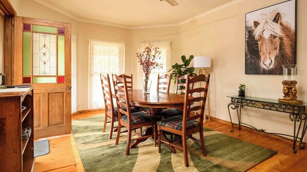 Un comedor con una mesa de madera, cuatro sillas, un florero con flores y un cuadro de un caballo en la pared.