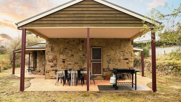 A stone building with a covered patio, outdoor seating, and a barbecue area.