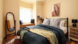 A bedroom with a large bed, a bedside table, a nightstand, a mirror, and a window with curtains.