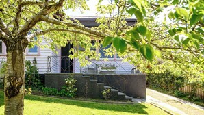 Een woongebouw met een stenen trap naar een veranda, omringd door weelderige beplanting en een verzorgd gazon.