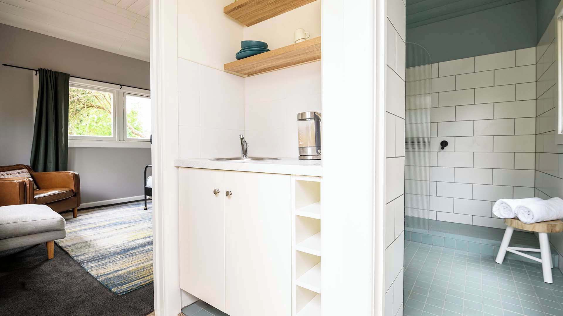 A modern bathroom with white tiles, a shower area, and a small stool with towels.