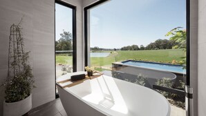 Une salle de bain moderne dotée d’une grande baignoire, offrant une vue sur une piscine et donnant sur un jardin.