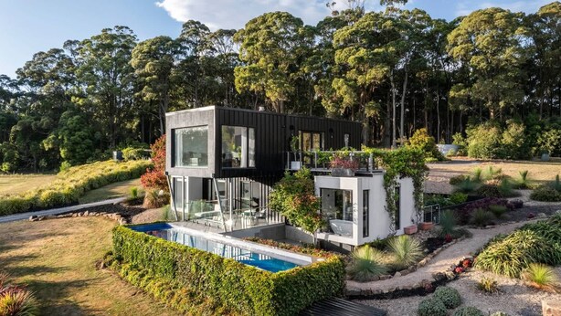 Une maison moderne à deux étages avec une piscine, entourée d’une végétation luxuriante et d’arbres.