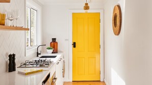 A kitchen with a yellow door, a window with glasses, a plant, and a book titled "OTTO LENGHI SIMPLE".