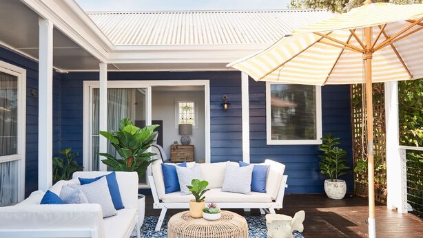 A blue house with a covered patio, white furniture, and a striped umbrella.