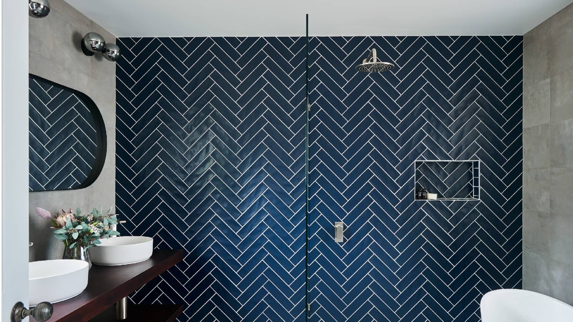A bathroom with a herringbone patterned wall, a round mirror, a white sink, and a shower area.