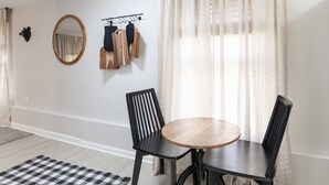 Une pièce comprenant une table ronde en bois, deux chaises noires, un miroir et un porte-manteau sur lequel sont suspendus des vêtements.