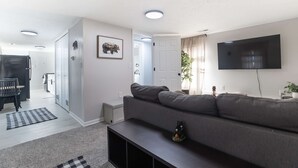 Un salon moderne comprenant un canapé, un téléviseur à écran plat, un coin repas avec une table et des chaises, et un couloir menant à une autre pièce.