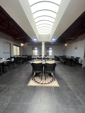 A spacious conference room with a high ceiling and skylight, featuring multiple tables and chairs arranged for meetings. - Le Ideal Suites (Puducherry)