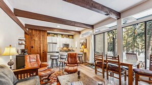 A spacious living area with a fireplace, leather chairs, a coffee table, and a view of the kitchen and dining area.