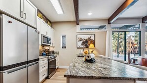 A modern kitchen with stainless steel appliances, a marble countertop, and a large window offering a view of the outdoors.