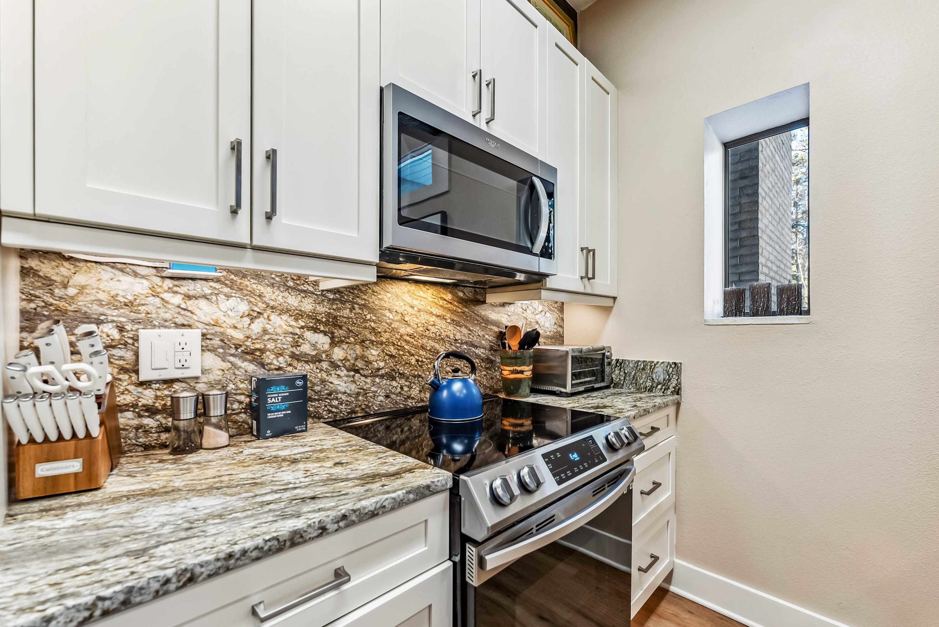 A kitchen with white cabinets, a microwave, a stove, and a granite countertop.