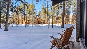 A covered outdoor seating area with wooden chairs and tables, surrounded by snow-covered ground and tall trees.