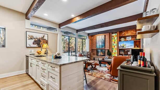 A modern kitchen with a central island, wooden beams, and a fireplace.