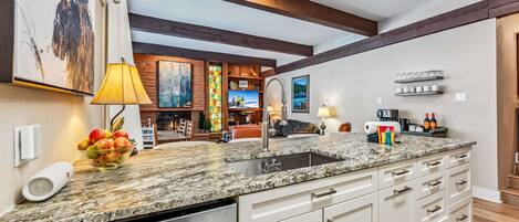 A kitchen with granite countertops, white cabinets, a built-in dishwasher, and a large window.