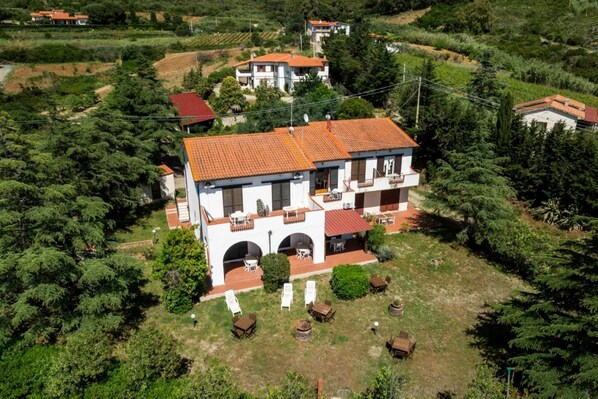 A two-story house with a red-tiled roof, a balcony, and a small garden with outdoor furniture.