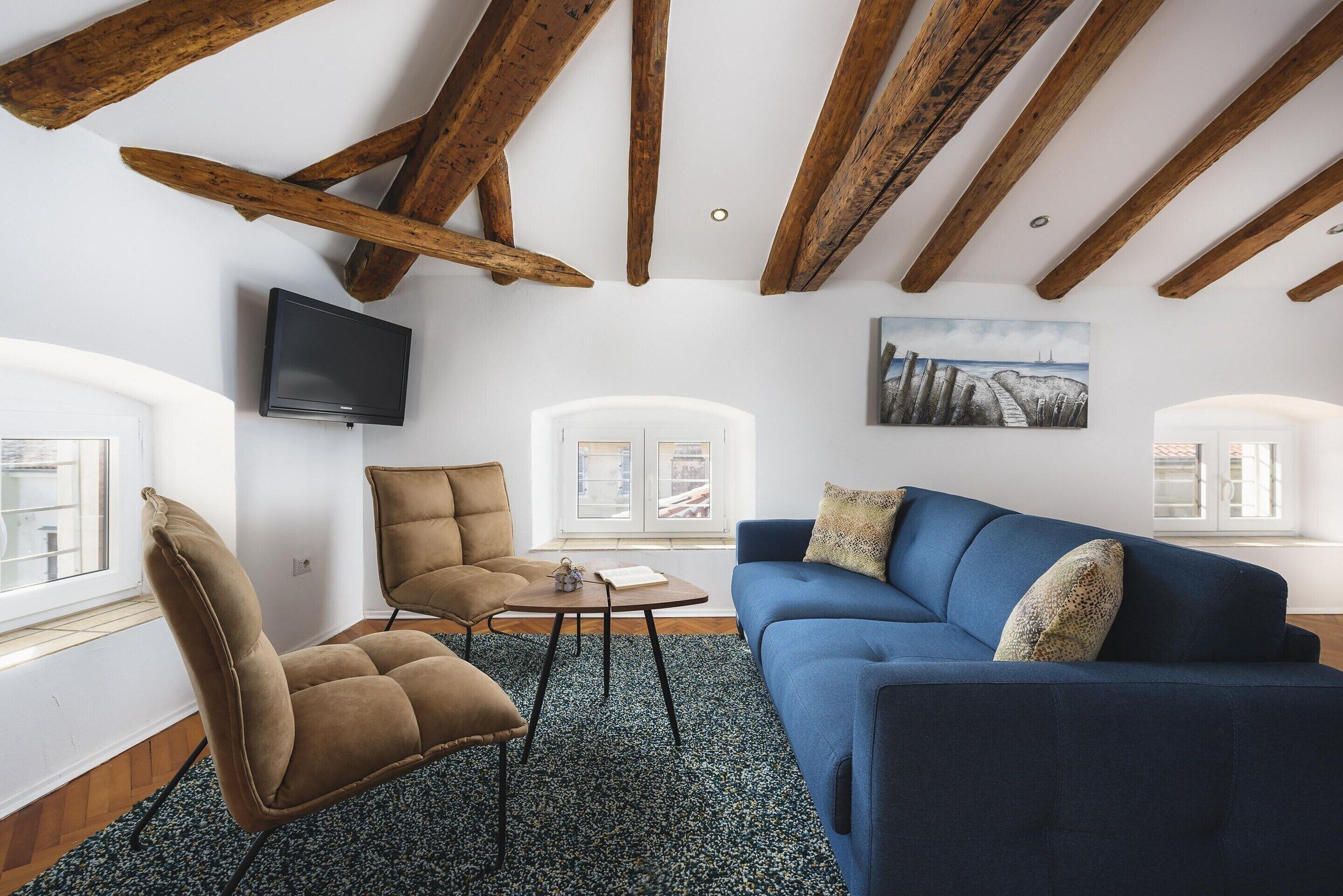 A living room with a blue sofa, a brown armchair, a small round table, and a television mounted on the wall.
