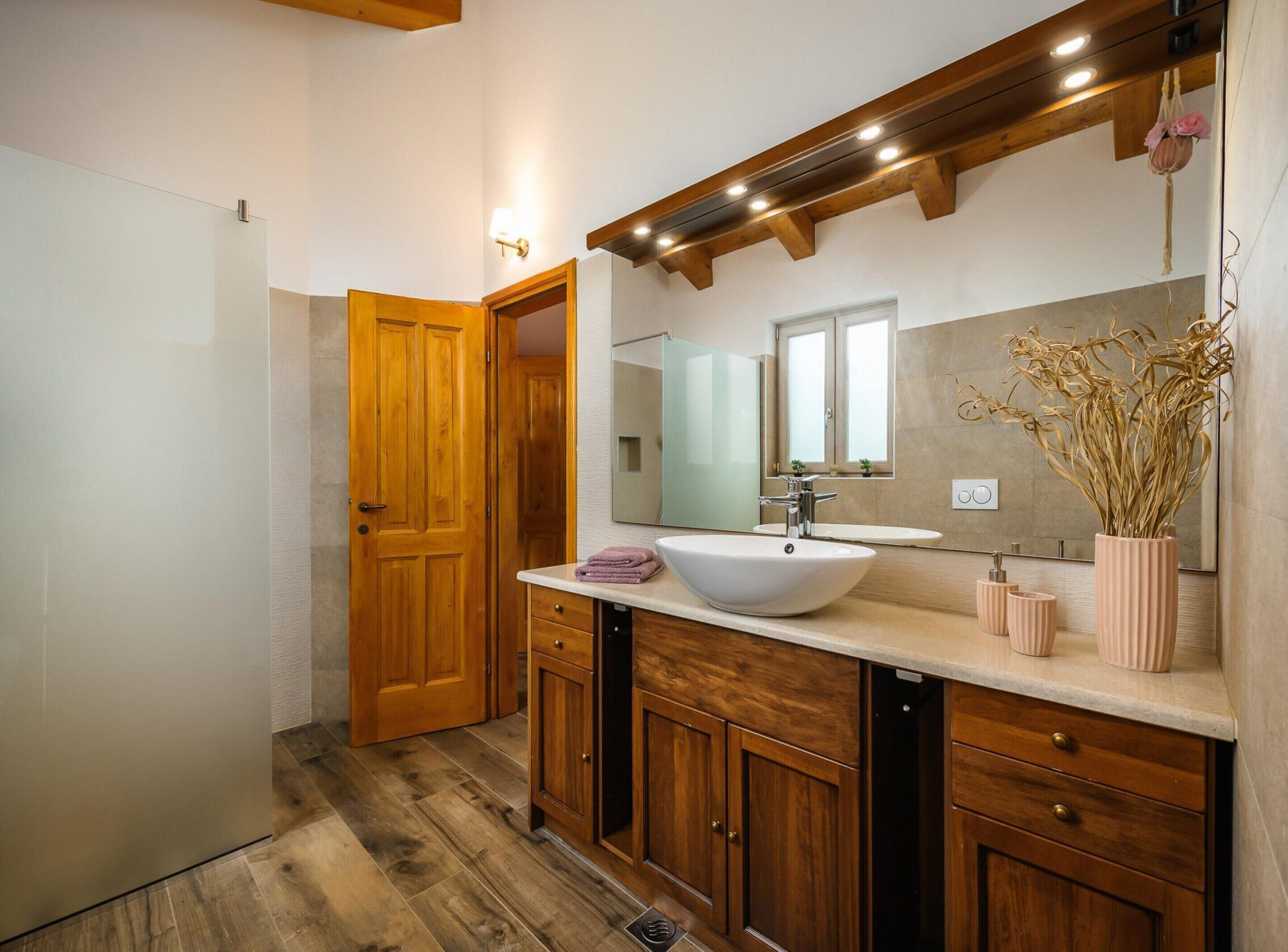 Une salle de bain moderne avec un meuble-lavabo en bois, un grand miroir et un lavabo sur colonne blanc.