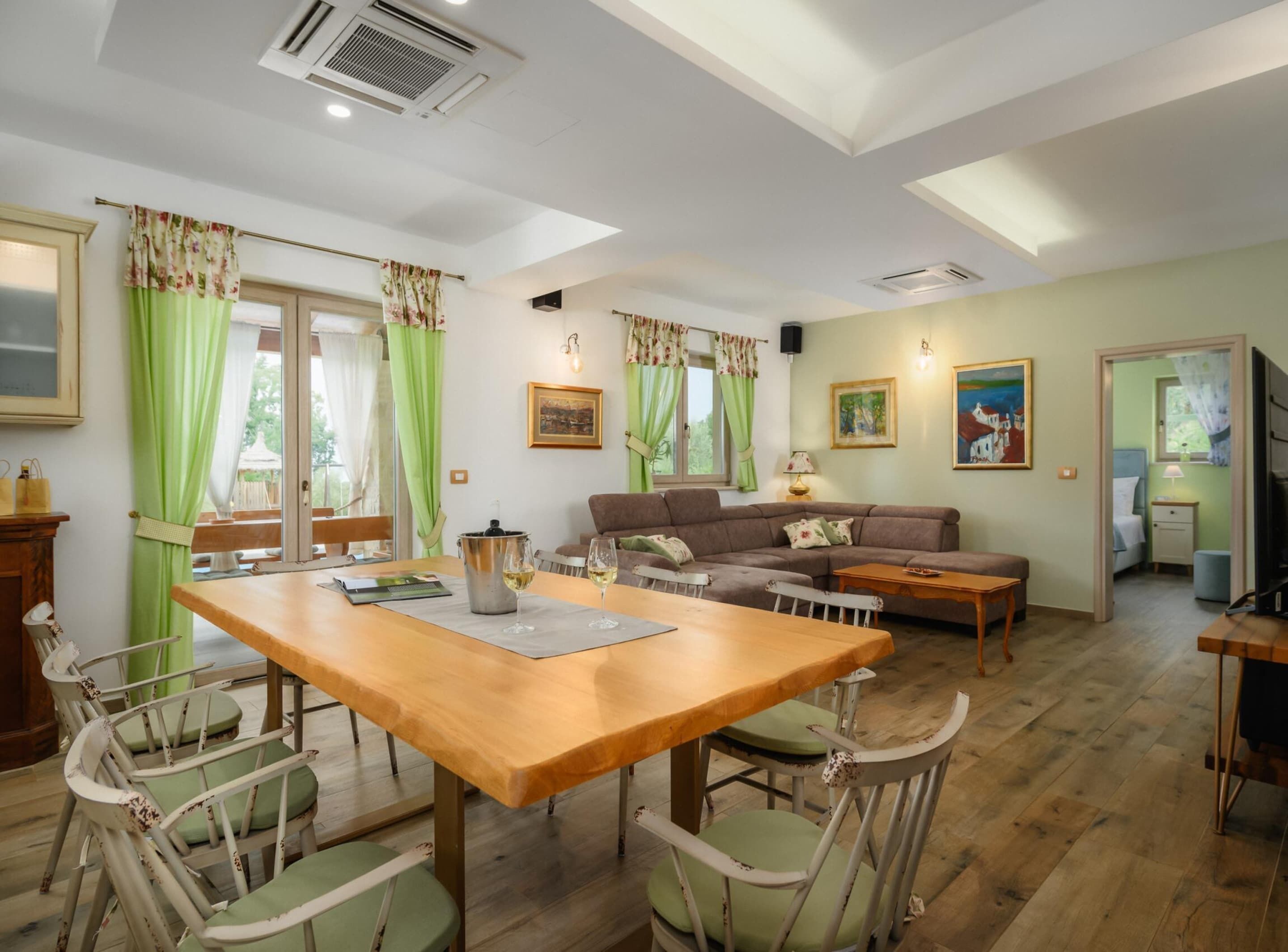 A cozy living room with a wooden dining table, green chairs, a sofa, and a television.