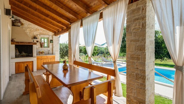 Une table à manger en bois avec des bancs, une cheminée en pierre et une vue sur une piscine.
