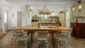 Une cuisine spacieuse avec un îlot central, une table à manger en bois et des chaises d’époque.