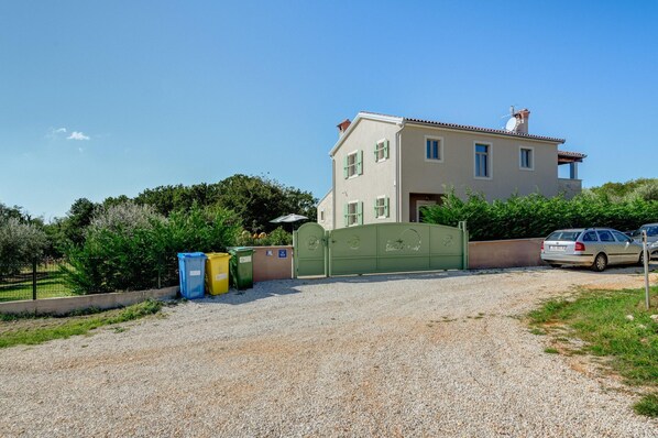 Une maison à deux étages avec une allée en gravier, un portail vert et une voiture garée.
