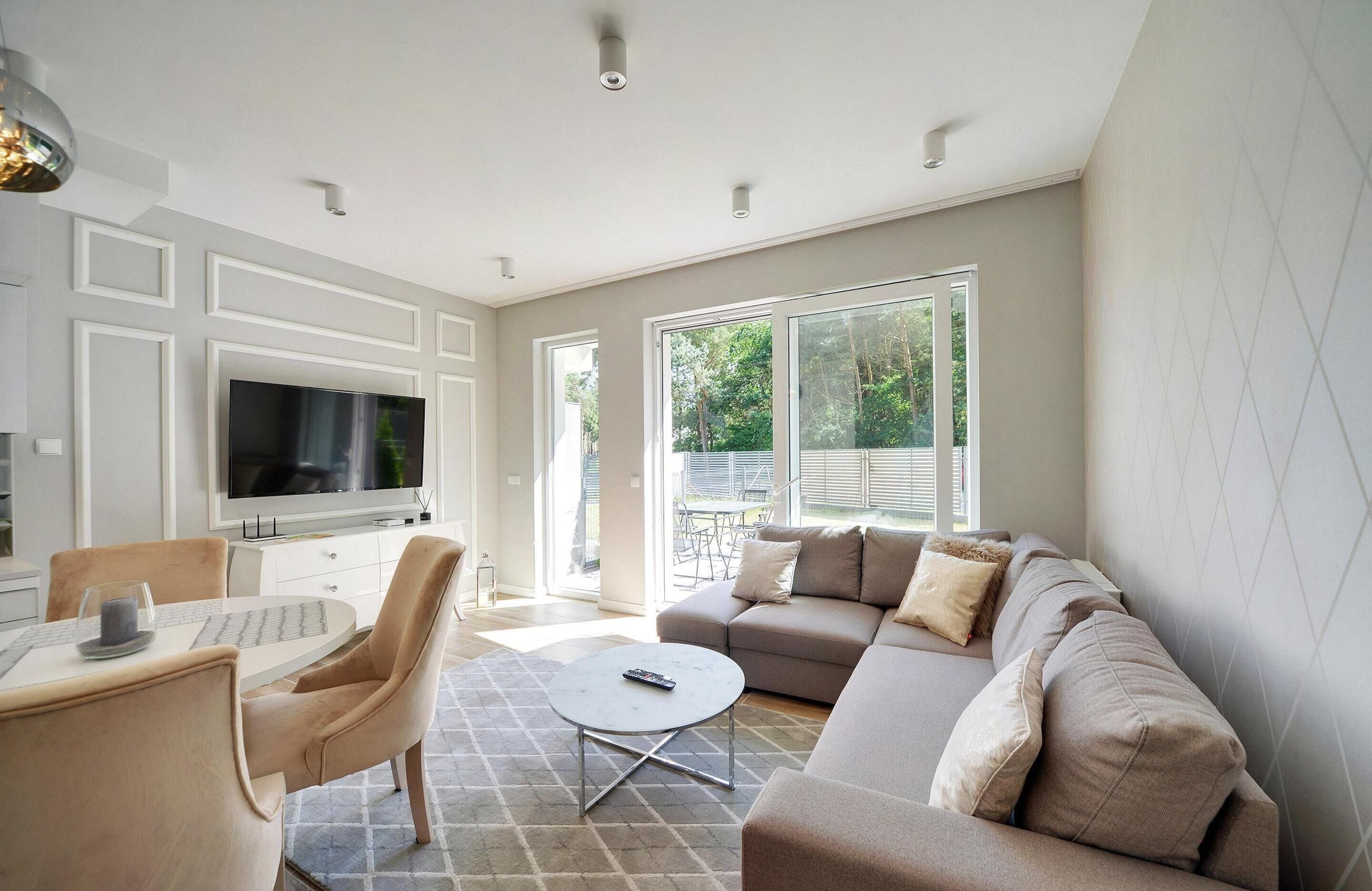 A modern living room with a large TV, a sofa, a coffee table, and a dining area with chairs.
