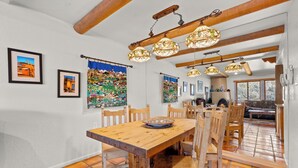 A dining area with a wooden table and chairs, hanging stained glass lights, and a view into another room with a fireplace. - Casa la Siesta | Serene Santa Fe Getaway (Santa Fe)